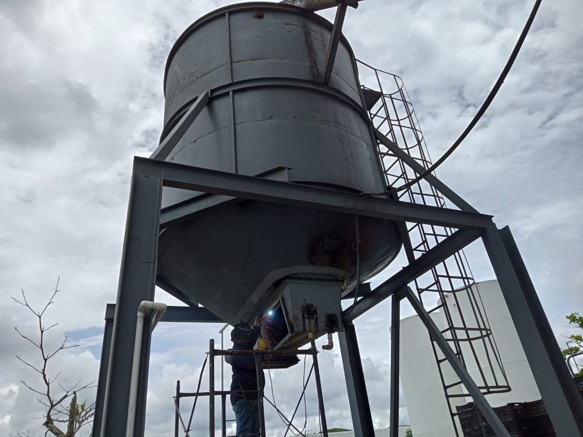 Tolva o silo metálico sobre estructura de acero con soldador trabajando